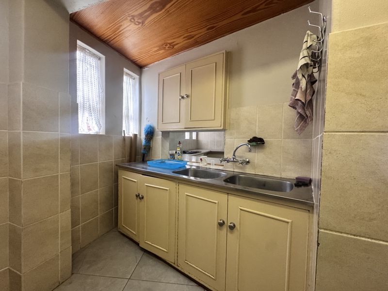A functional scullery area featuring double stainless steel sinks, built-in cabinetry, tiled splashbacks, and a timber-paneled ceiling.