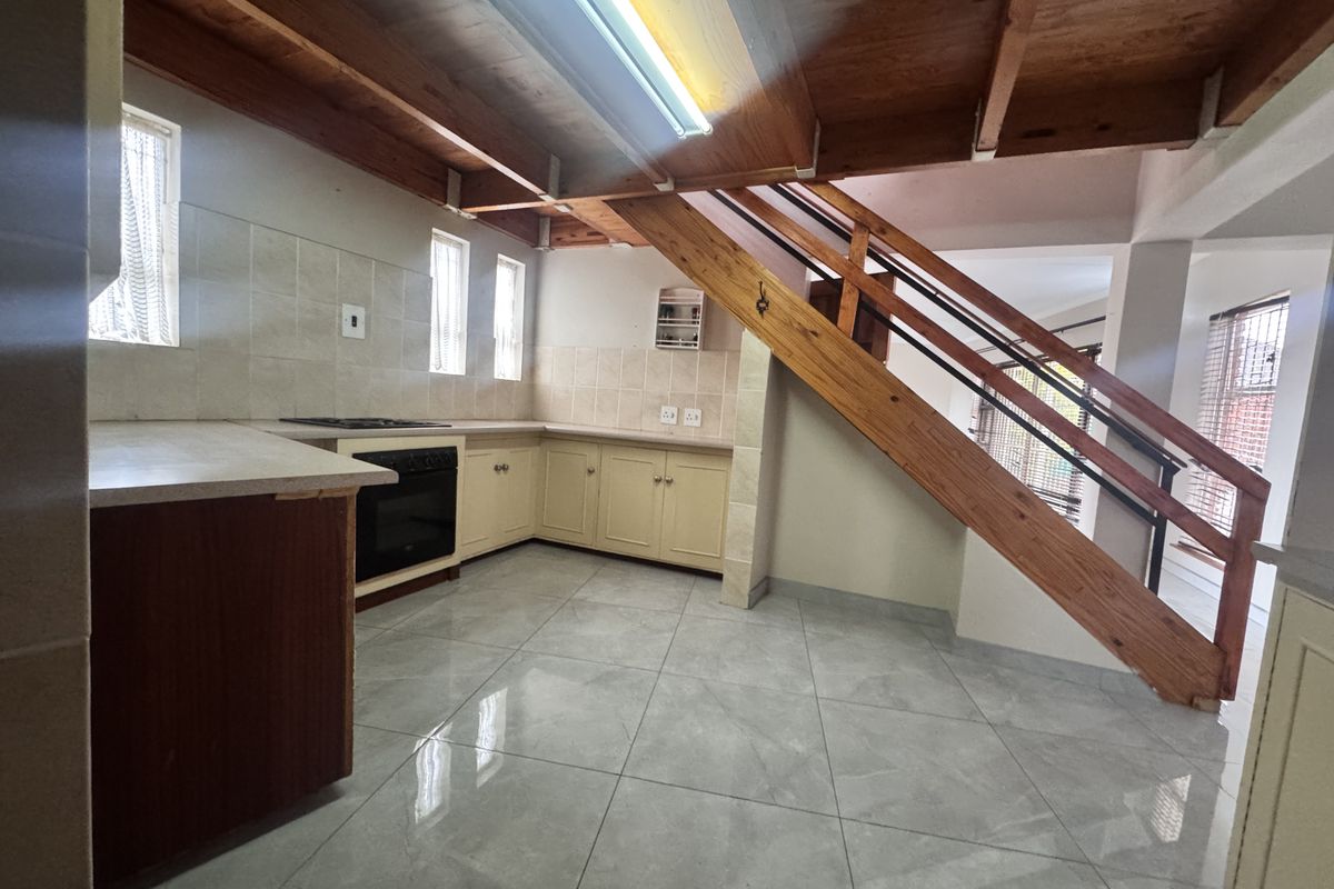 A functional kitchen featuring tiled flooring, built-in cabinetry, and an integrated oven, complemented by exposed timber ceiling beams and an adjacent staircase.
