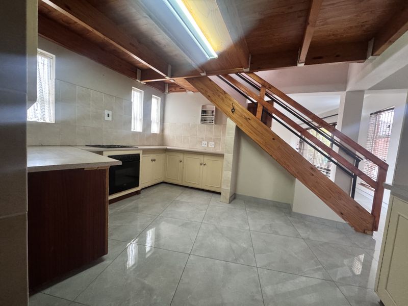 A functional kitchen featuring tiled flooring, built-in cabinetry, and an integrated oven, complemented by exposed timber ceiling beams and an adjacent staircase.