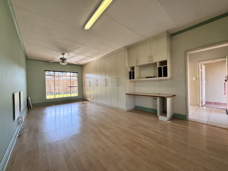 Spacious bedroom featuring extensive built-in cabinetry, a dedicated desk area, laminate flooring, and a ceiling fan, offering a versatile layout for living or work.
