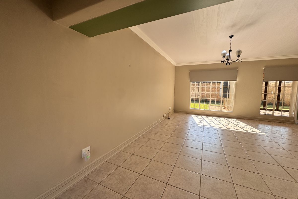 A spacious, sunlit living area featuring neutral ceramic tile flooring, classic cove cornicing, and large multi-pane windows with access to the garden.