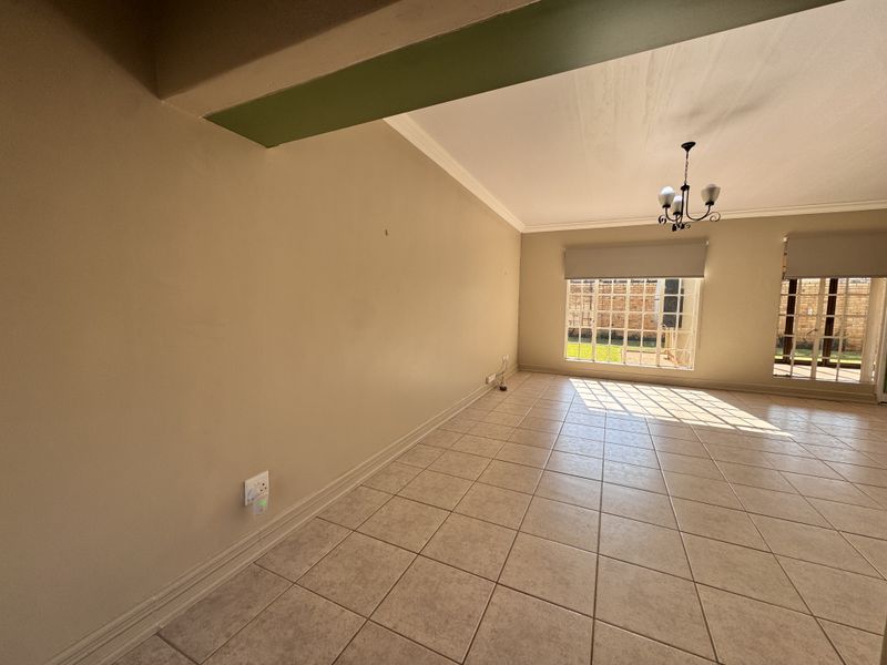 A spacious, sunlit living area featuring neutral ceramic tile flooring, classic cove cornicing, and large multi-pane windows with access to the garden.