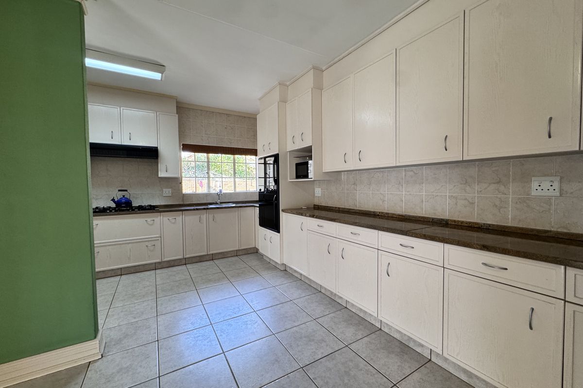Spacious kitchen featuring ample built-in cabinetry, stone countertops, tiled backsplash, and integrated appliances including a gas hob and oven.