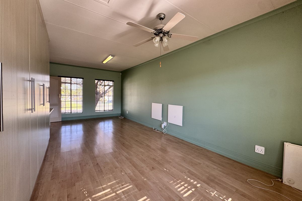 Spacious bedroom featuring laminate flooring, extensive built-in cupboards, a ceiling fan, and wall-mounted panel heaters for climate control.