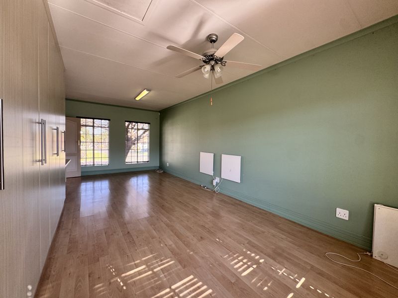 Spacious bedroom featuring laminate flooring, extensive built-in cupboards, a ceiling fan, and wall-mounted panel heaters for climate control.