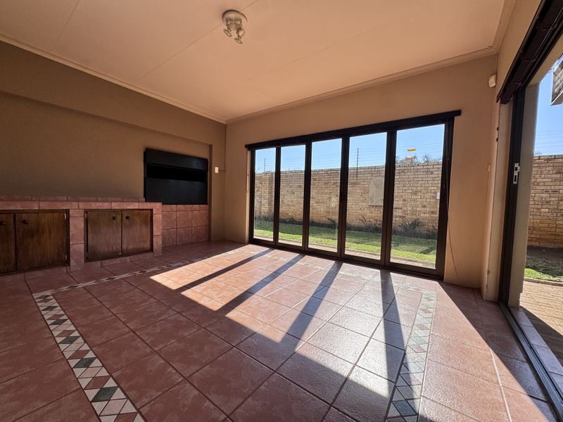 Spacious covered patio featuring a built-in braai, tiled flooring, and large sliding glass doors opening to the rear garden area.