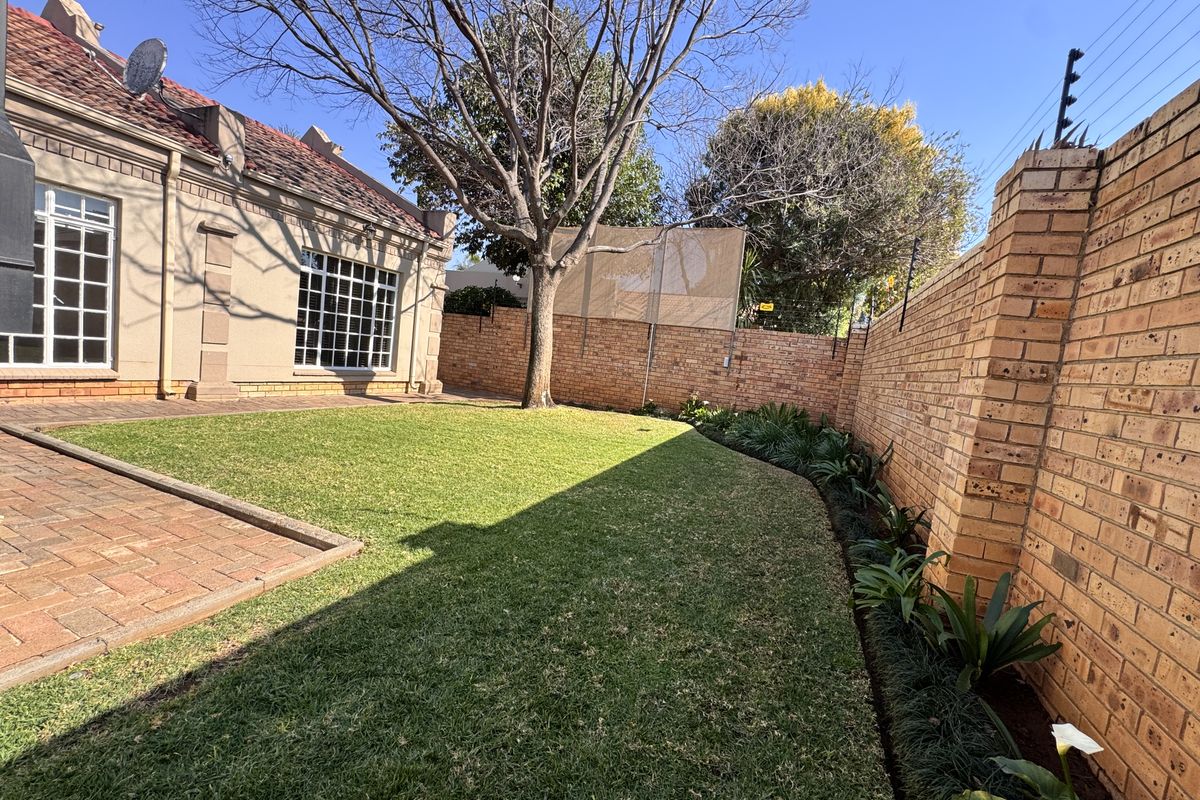 A well-maintained rear garden featuring a paved patio area, established lawn, and secure brick boundary walls with electric fencing.