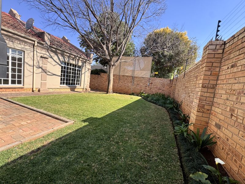 A well-maintained rear garden featuring a paved patio area, established lawn, and secure brick boundary walls with electric fencing.