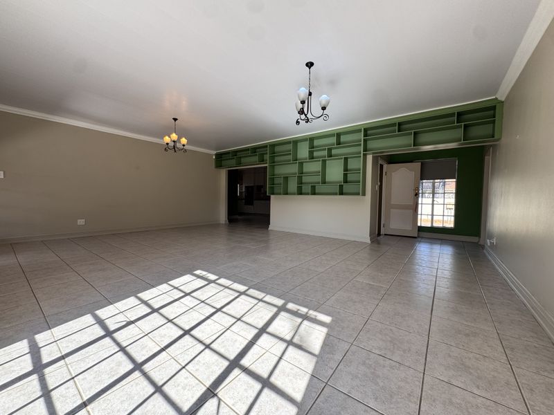 Spacious living area featuring neutral tiled flooring, built-in green shelving, and classic wrought iron chandeliers, offering a bright and open layout.