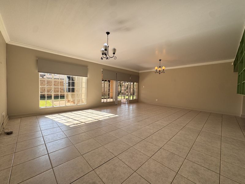 Spacious, light-filled living area featuring neutral tiled flooring, built-in shelving, and large windows with direct access to the outdoor patio area.