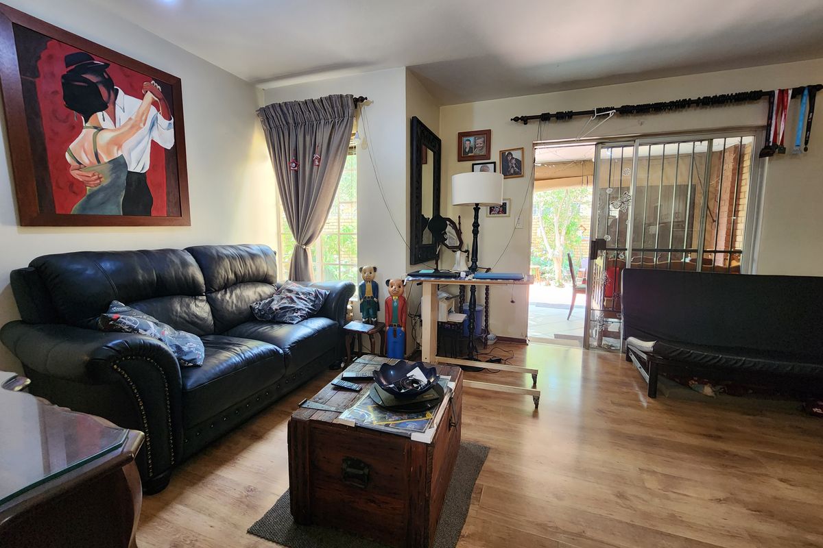 A living room featuring laminate flooring and a sliding glass door with a security gate, providing direct access to the outdoor patio area.