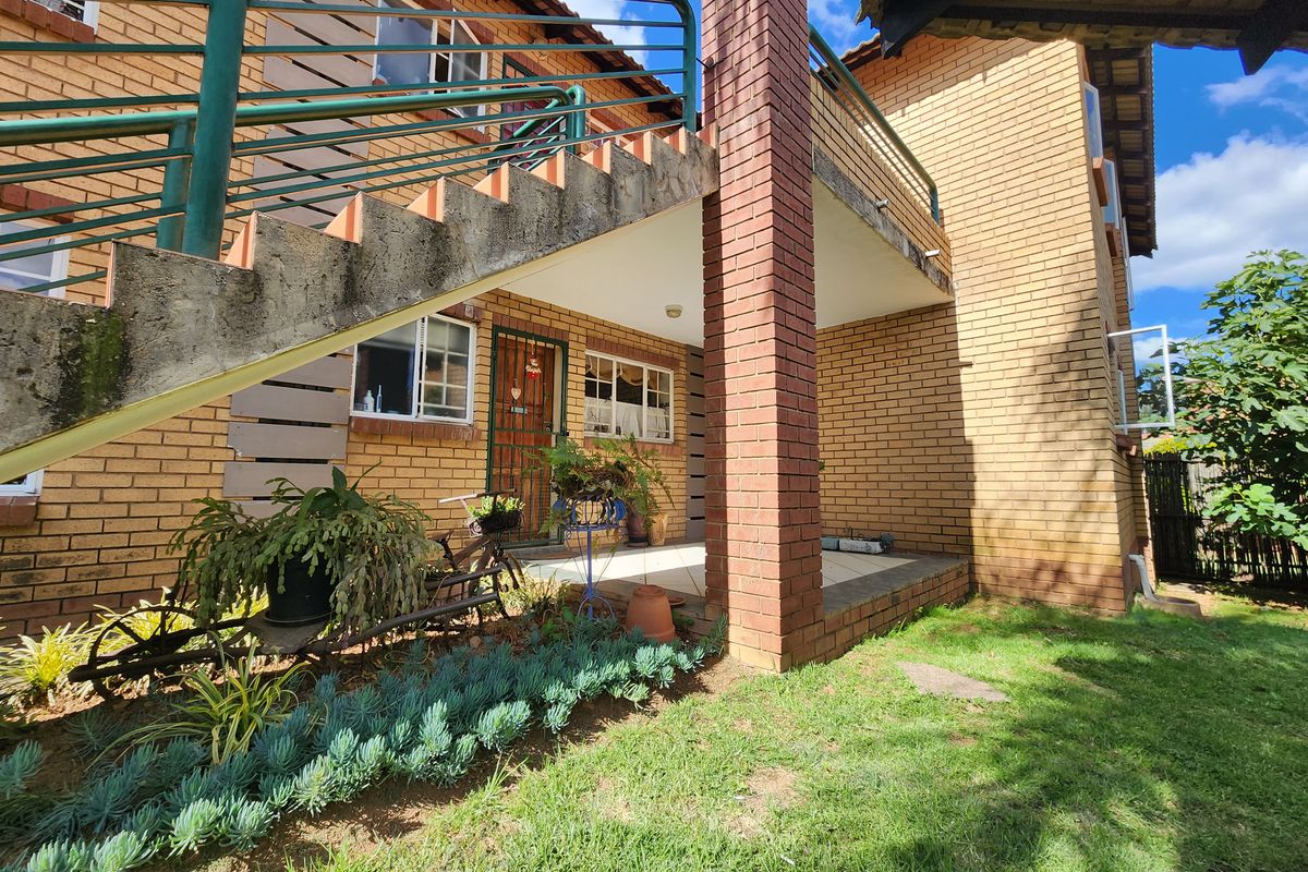 Rear exterior view of the townhouse featuring a brick facade, a covered patio area, and an external concrete staircase with metal railings.