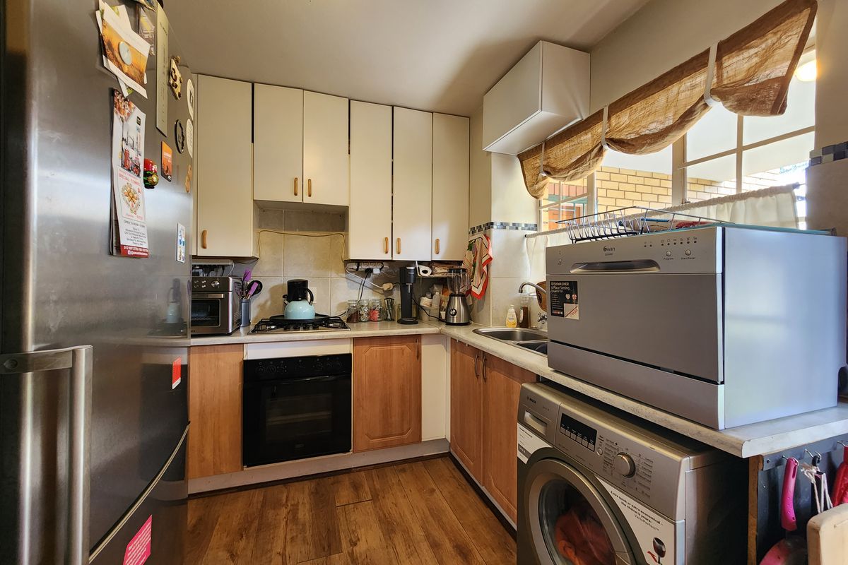 A compact kitchen featuring wood-tone and white cabinetry, laminate countertops, a built-in oven with gas hob, and a stainless steel sink.
