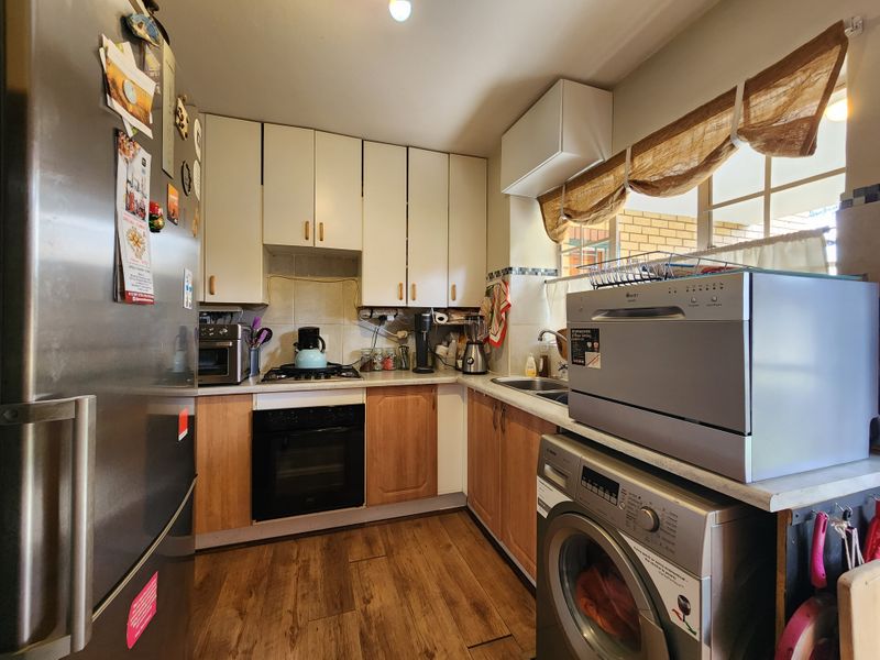 A compact kitchen featuring wood-tone and white cabinetry, laminate countertops, a built-in oven with gas hob, and a stainless steel sink.