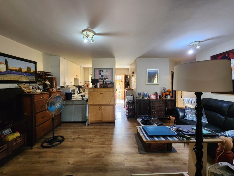 Open plan living area featuring laminate flooring and a functional kitchen space with built-in cabinetry, leading towards a rear exterior entrance.