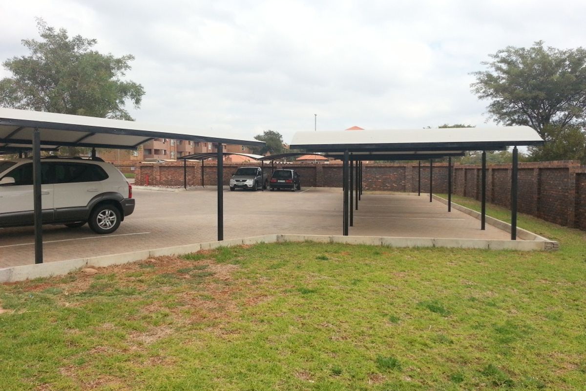 An outdoor parking area featuring covered carports with a paved surface and secure brick boundary walling.