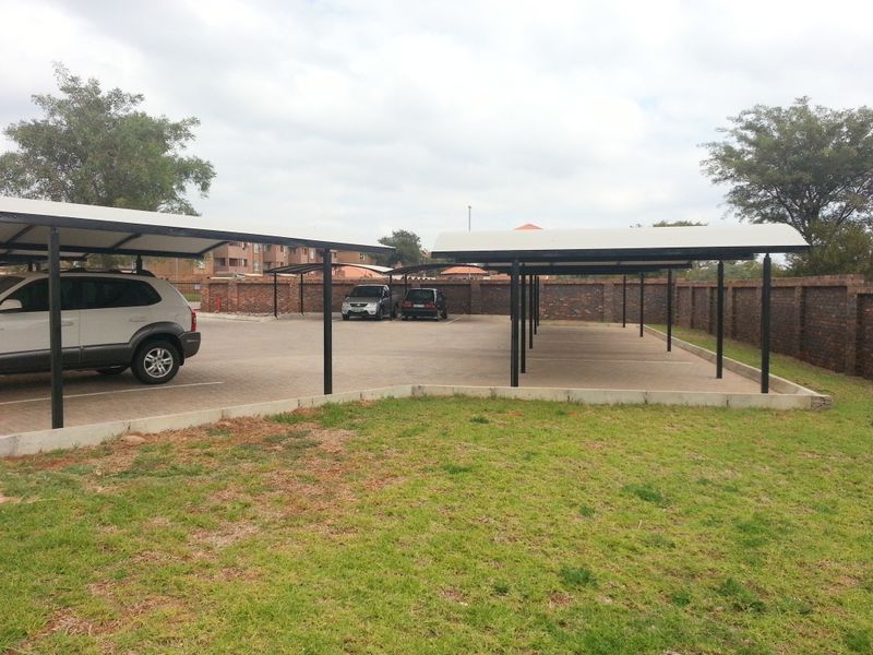 An outdoor parking area featuring covered carports with a paved surface and secure brick boundary walling.