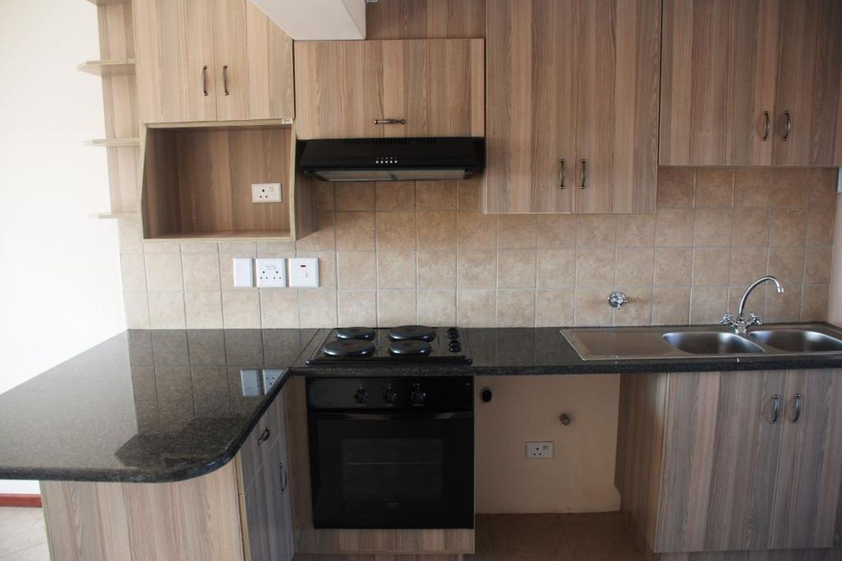 A functional kitchen featuring wood-look laminate cabinetry, granite countertops, a built-in oven with hob, and a tiled backsplash.