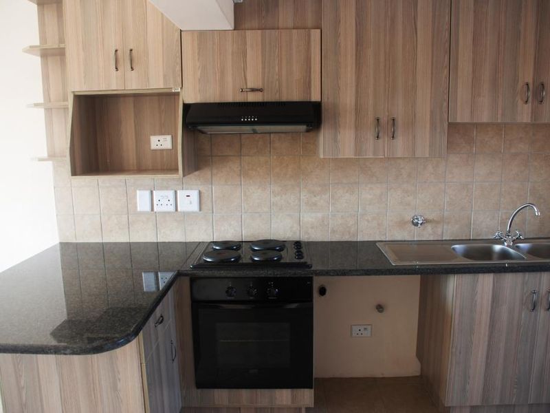 A functional kitchen featuring wood-look laminate cabinetry, granite countertops, a built-in oven with hob, and a tiled backsplash.