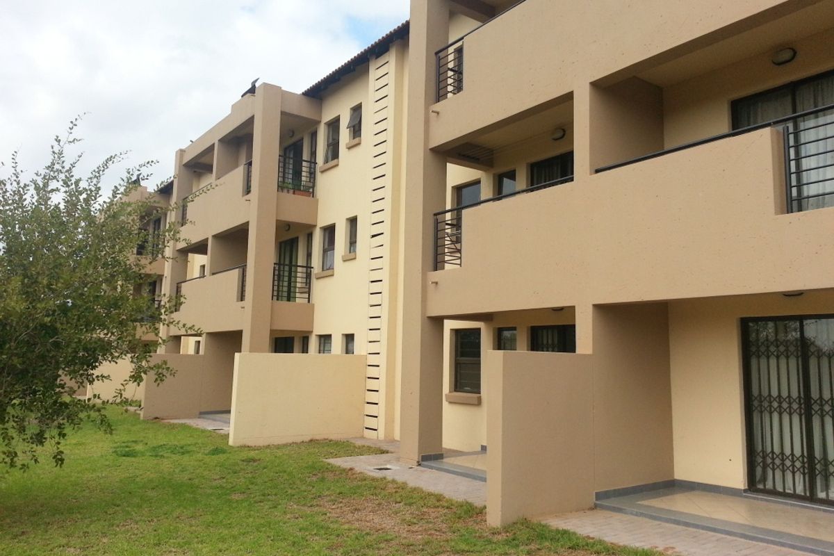 Rear view of a multi-story apartment complex featuring private balconies, ground-floor patios, and security gates on sliding glass doors.