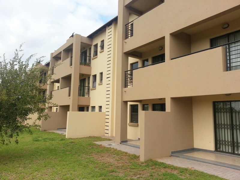 Rear view of a multi-story apartment complex featuring private balconies, ground-floor patios, and security gates on sliding glass doors.