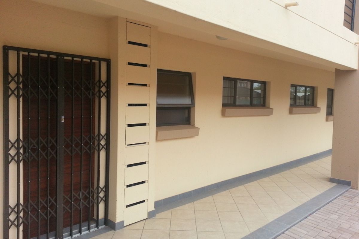 Exterior view of an apartment entrance featuring a security gate, tiled walkway, and aluminium window frames.