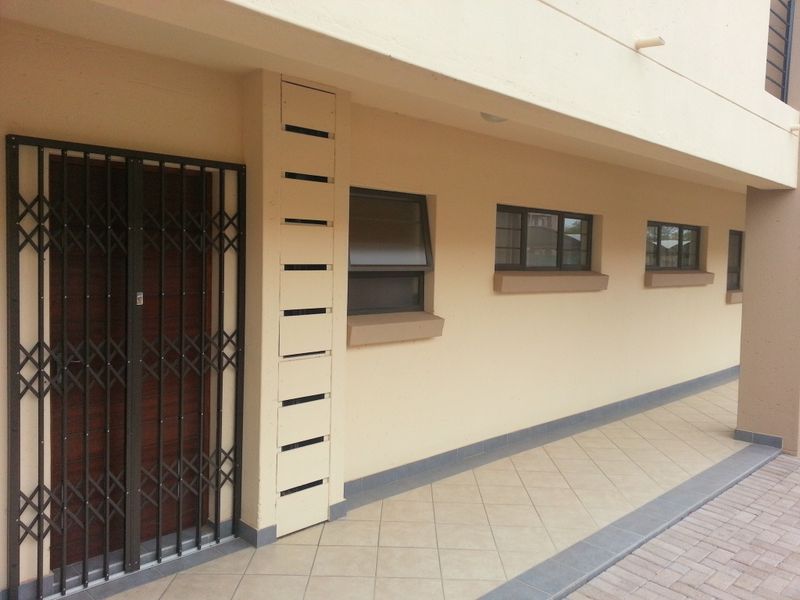 Exterior view of an apartment entrance featuring a security gate, tiled walkway, and aluminium window frames.