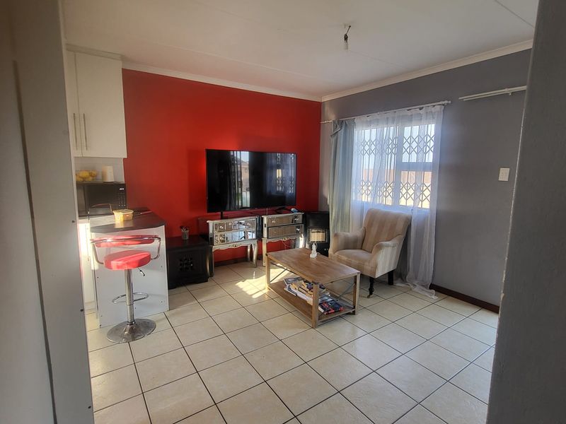 Open-plan living area featuring tiled flooring, a compact kitchen section, and a window fitted with a security gate.