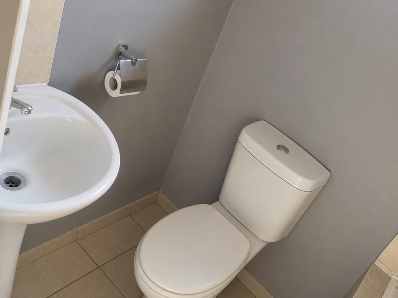 A clean and functional bathroom featuring a white pedestal basin, a modern toilet, and neutral floor tiling.