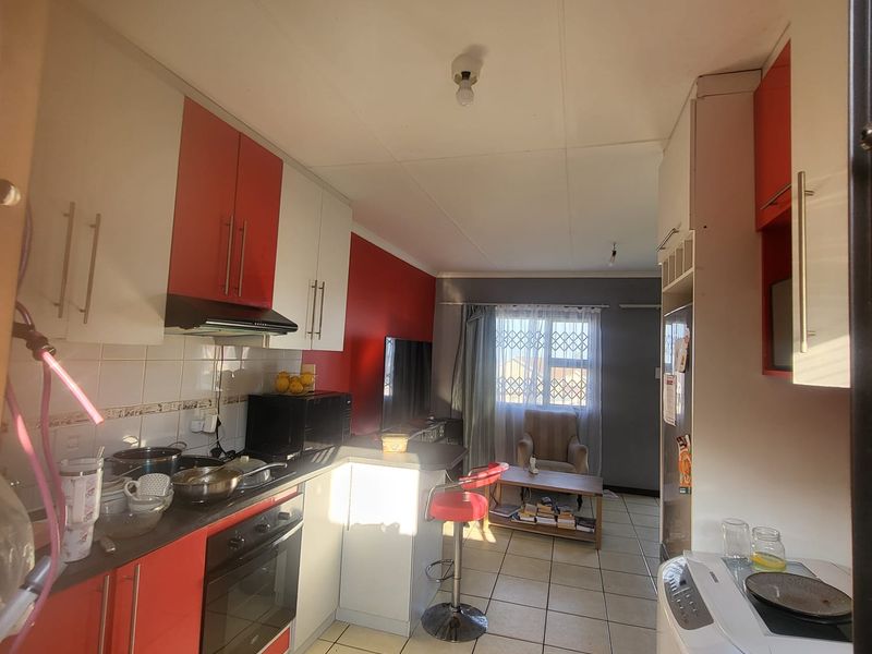 Open-plan kitchen and living area featuring red and white cabinetry, built-in oven, extractor fan, and tiled flooring throughout.