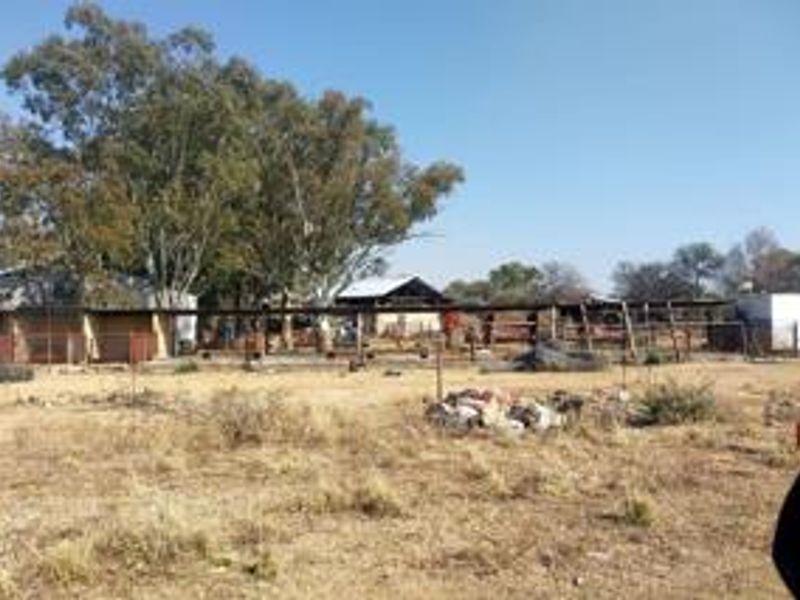 View of the rear property grounds featuring various outbuildings, fencing, and open land area requiring maintenance and clearing.