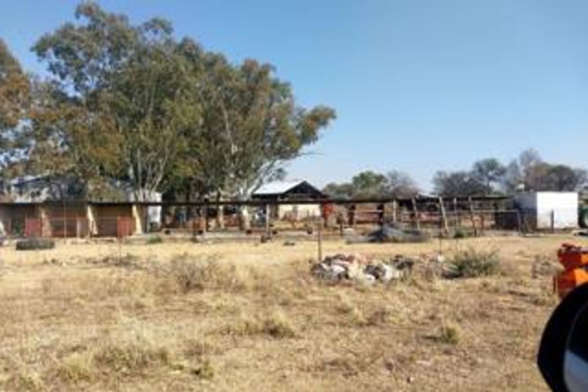 View of the rear property grounds featuring various outbuildings, fencing, and open land area requiring maintenance and clearing.