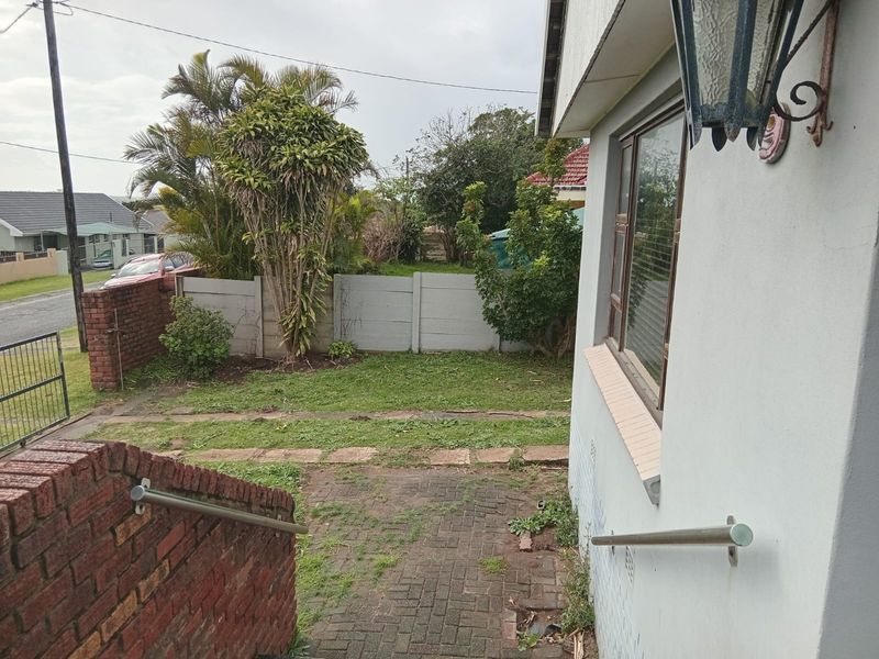 Front exterior view showing a paved entrance area, brick boundary wall, and small garden space with established trees.