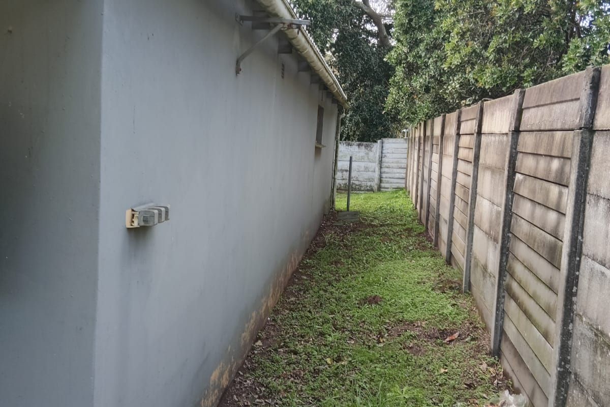 A narrow side passage of the property featuring a precast concrete boundary wall and exterior wall with guttering.
