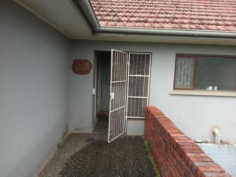 Entrance area featuring a security gate, tiled walkway, and brick retaining wall, showing signs of wear and maintenance requirements.