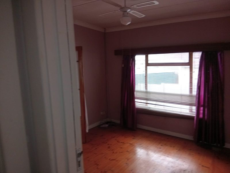 A vacant bedroom featuring polished timber flooring, a ceiling fan, and a large window with fitted venetian blinds.