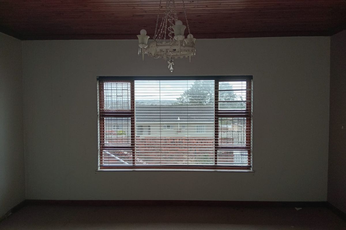 An empty bedroom featuring a timber ceiling, a central chandelier, and a large window with fitted venetian blinds and security bars.