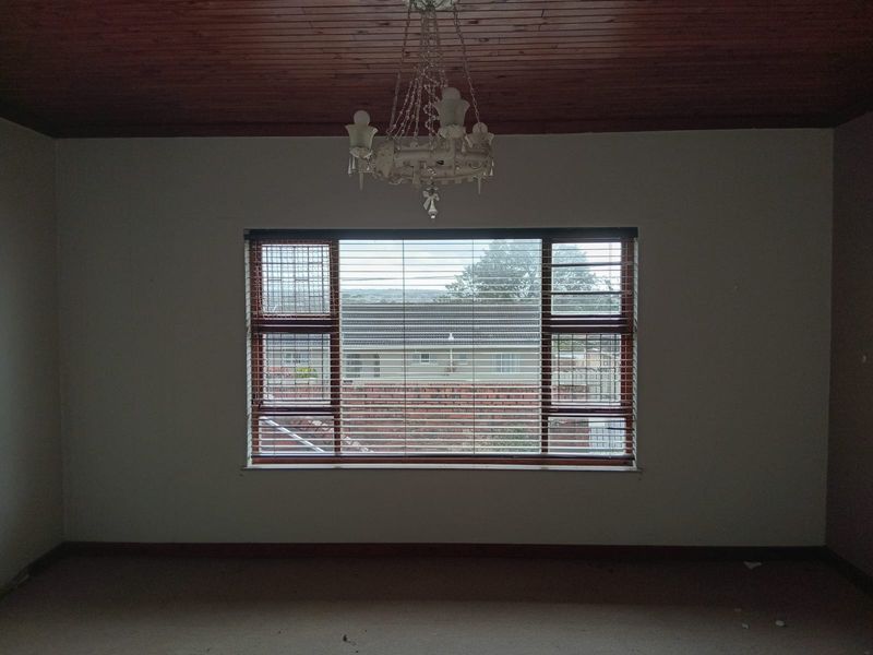 An empty bedroom featuring a timber ceiling, a central chandelier, and a large window with fitted venetian blinds and security bars.