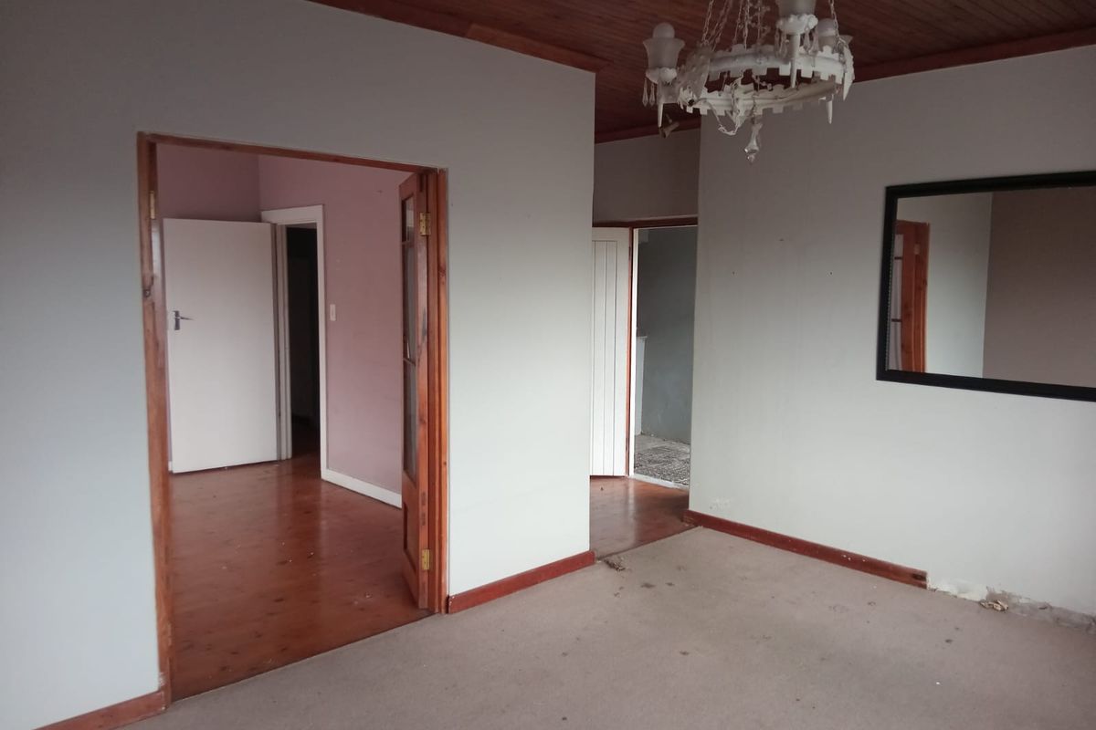 An empty living area featuring timber ceilings, wooden door frames, and a mix of timber and carpet flooring, offering a blank canvas for renovation.