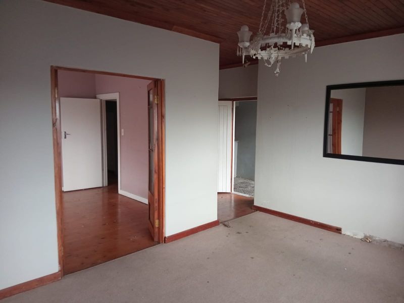 An empty living area featuring timber ceilings, wooden door frames, and a mix of timber and carpet flooring, offering a blank canvas for renovation.