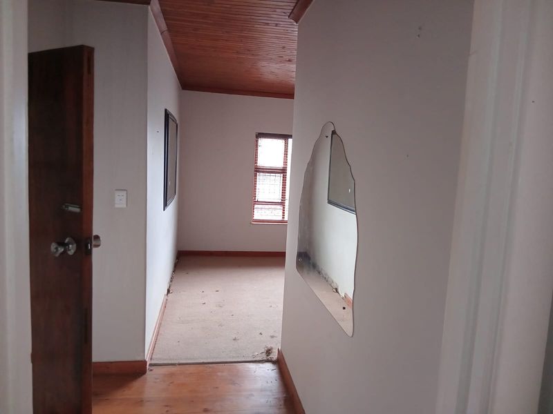 A vacant hallway featuring timber ceiling paneling, a mix of timber and carpet flooring, and a wooden door, showing signs of wear.