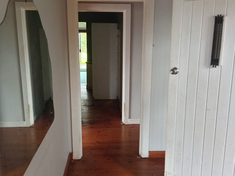 A vacant hallway featuring original timber flooring, white painted walls, and traditional door architraves, showing signs of wear and requiring cosmetic updates.