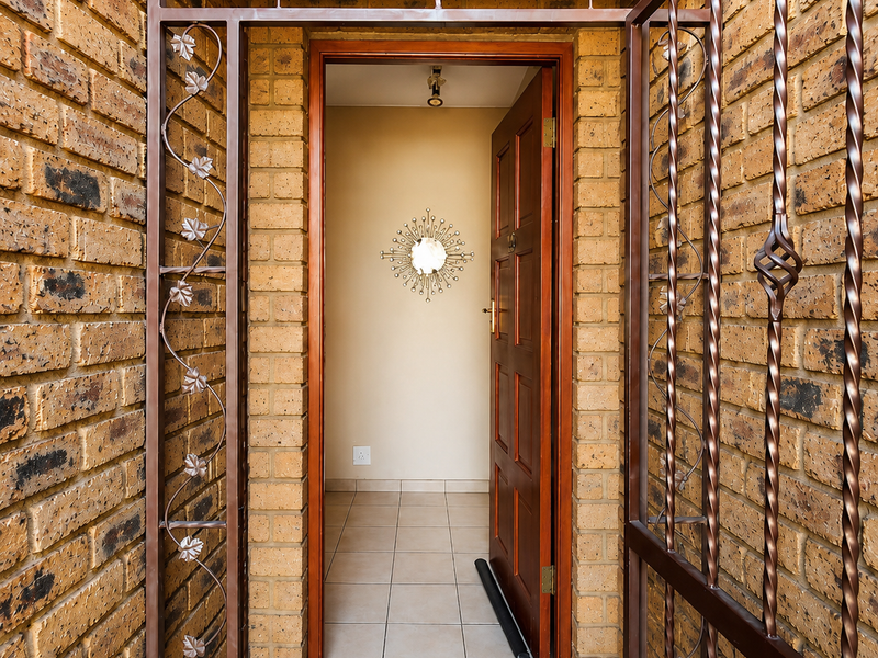 A secure entrance featuring a decorative metal security gate, face-brick exterior walls, and a solid wooden front door leading into a tiled foyer.