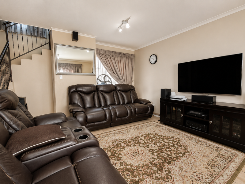 A comfortable living room featuring tiled flooring, a staircase with a wrought iron balustrade, and neutral wall finishes.