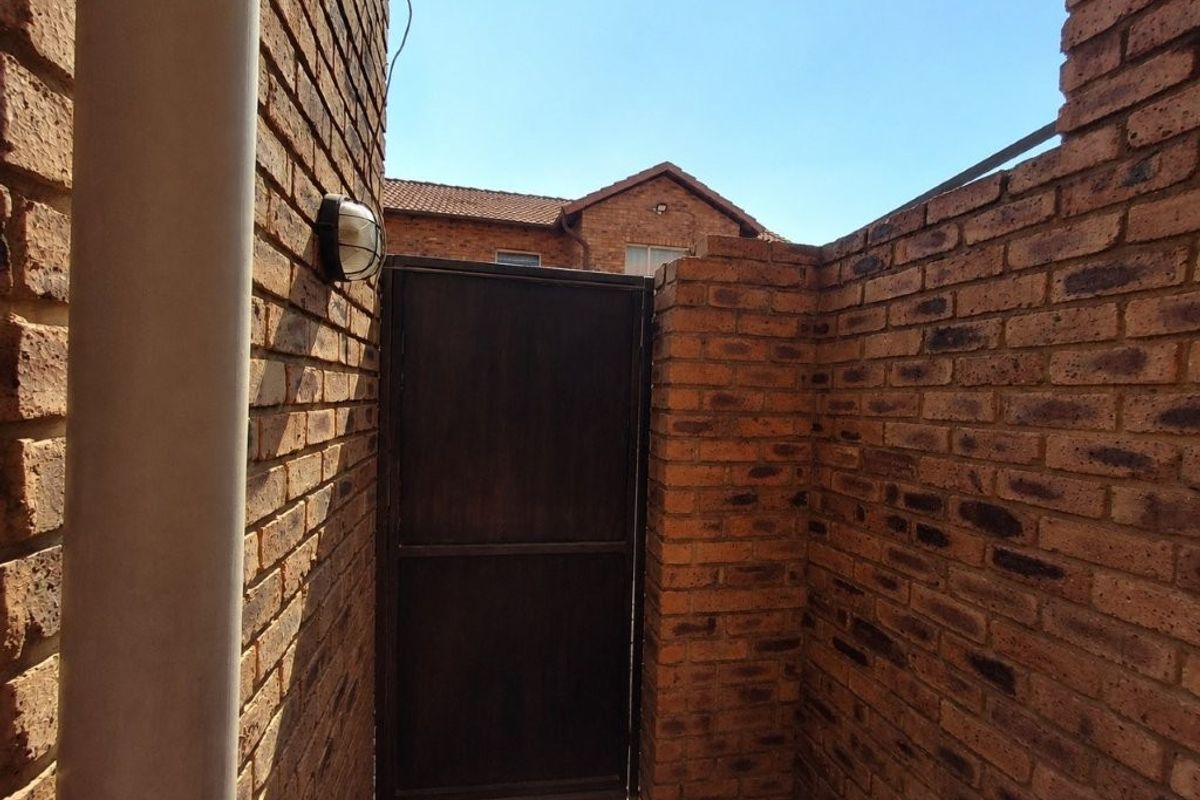 A secure rear courtyard area featuring exposed brick walls, a metal access gate, and an exterior wall-mounted light fixture.