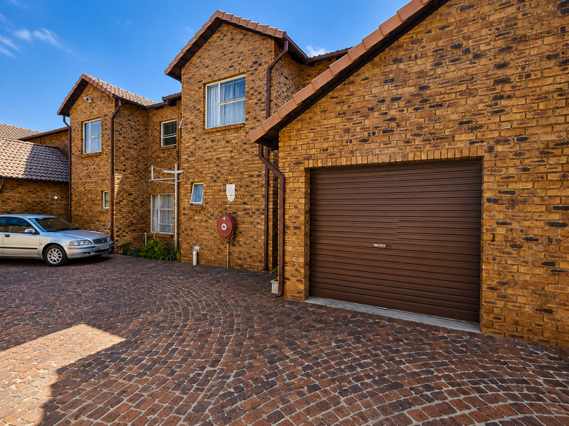 Front exterior view of a townhouse featuring a face brick facade, tiled roof, and a secure roller garage door with a paved driveway.