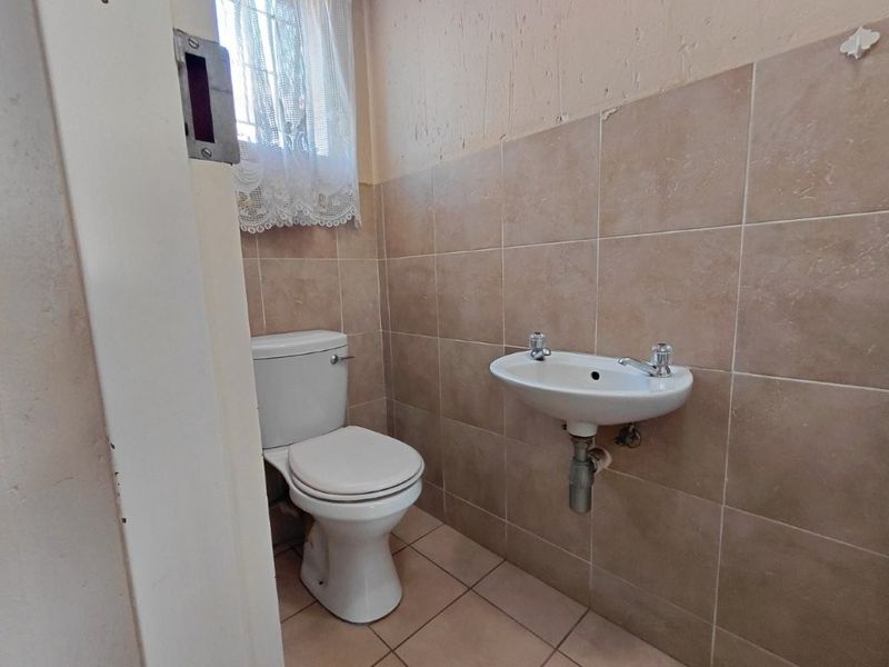 A compact guest bathroom featuring a wall-mounted basin and ceramic toilet with neutral wall and floor tiling.