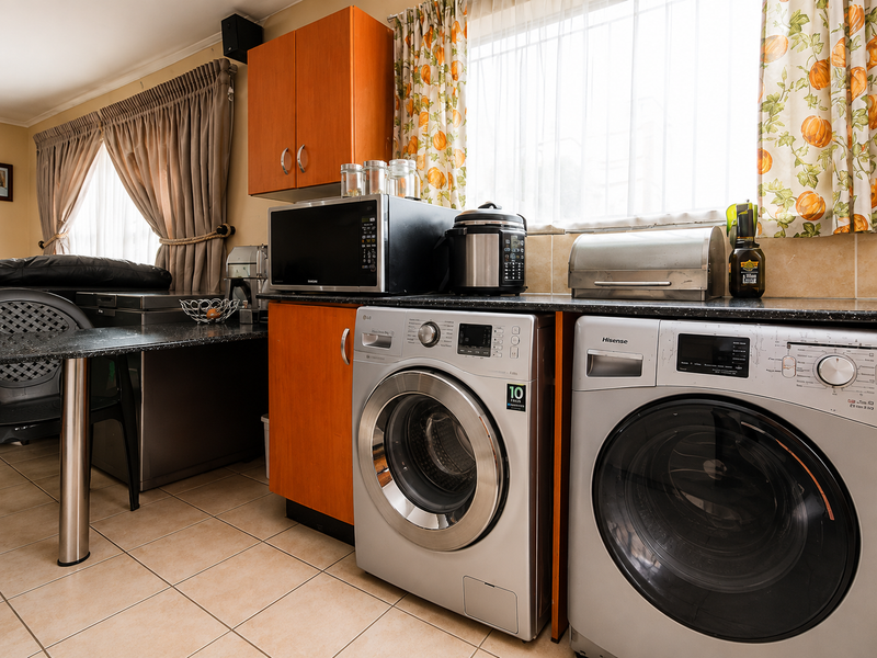 A functional laundry area featuring built-in cabinetry, granite countertops, and space for dual laundry appliances with tiled flooring.