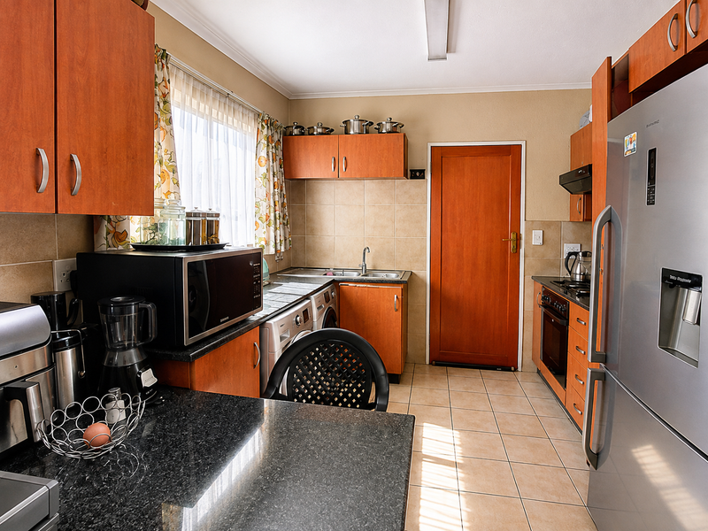 Functional kitchen featuring wood-finish cabinetry, granite countertops, tiled backsplash, and integrated appliances, offering a practical layout with direct access to an exterior door.