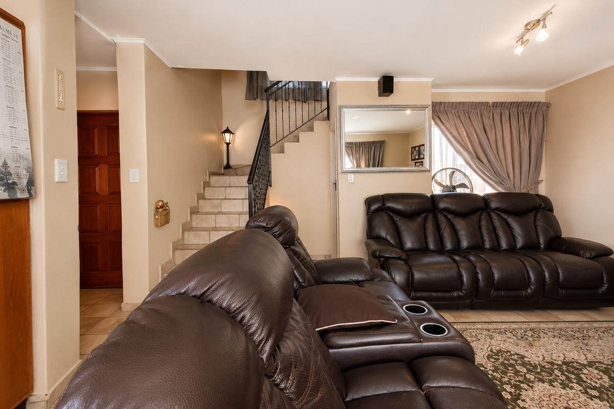 A comfortable living room featuring a staircase with a wrought iron balustrade, neutral wall tones, and tiled flooring throughout the space.